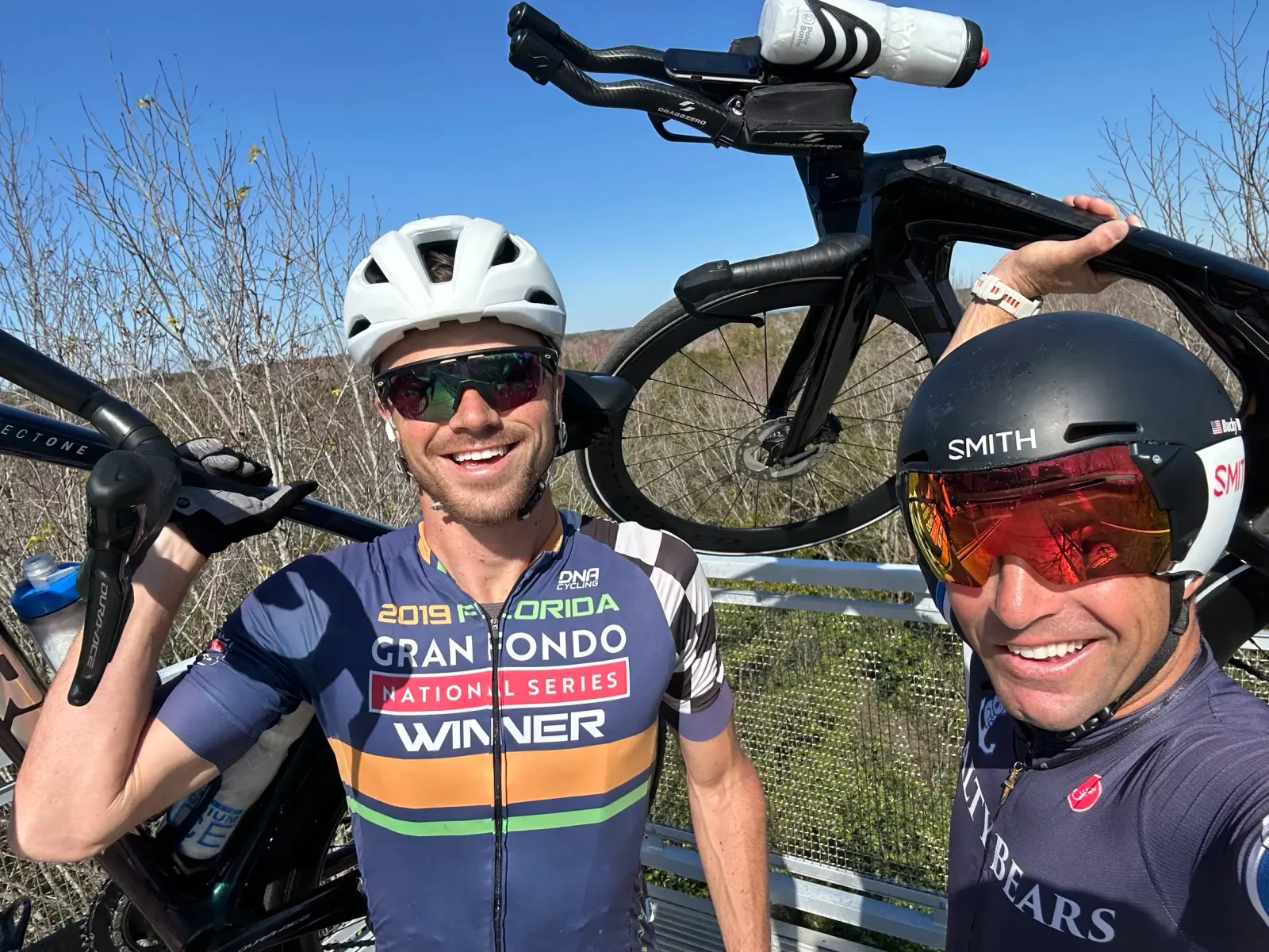 Two cyclists holding their bikes overhead and smiling